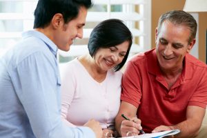 Financial Advisor Talking To Senior Couple At Home Signing Documents Smiling