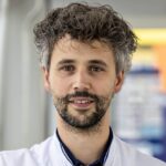 Jules Derks in white lab coat standing by a window.