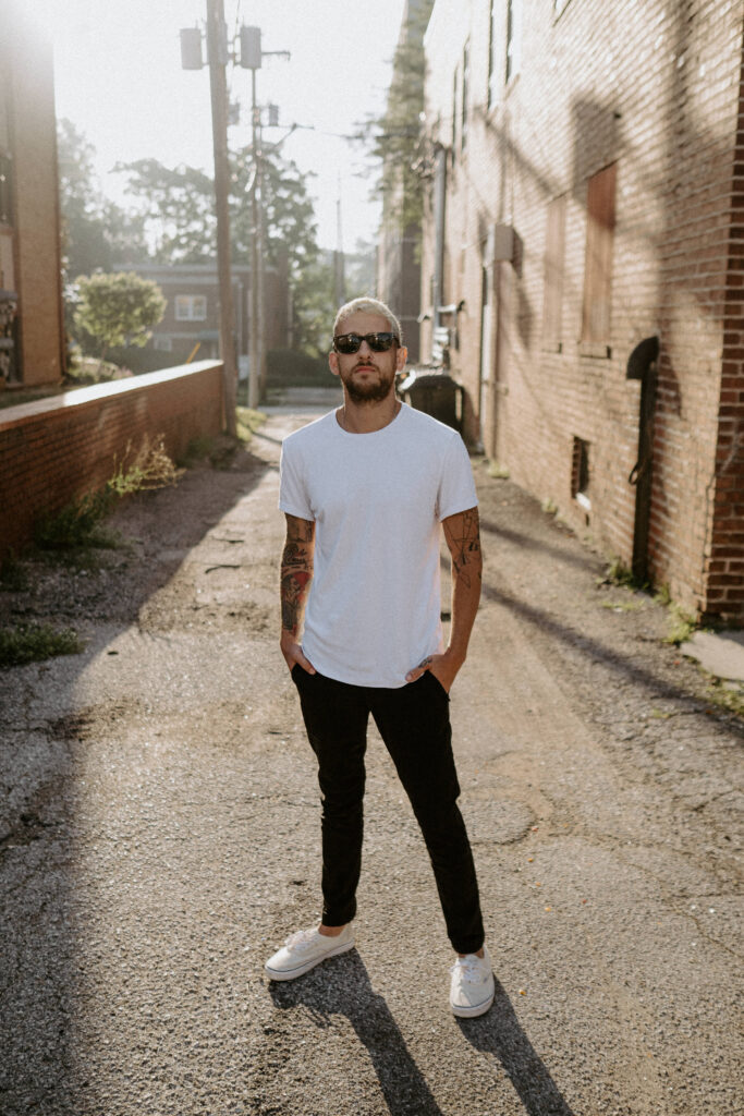 Jake Dawson standing alone with sunglasses on and hands in pockets.