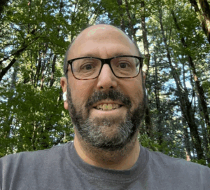 A man smiling while taking a selfie in the woods.