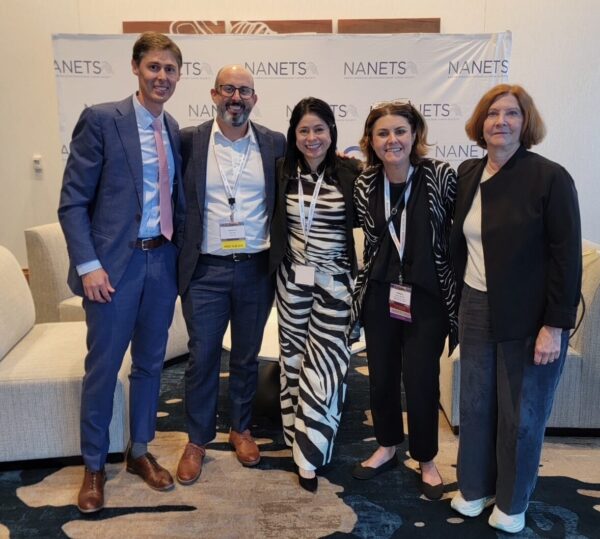 Five people standing and smiling in front of a branded screen.