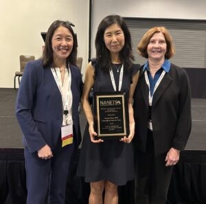 Woman standing between two other women holding a plaque and wearing a medal.