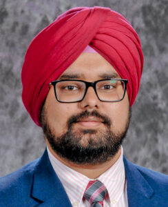 Man wearing red Sikh turban and glasses stares at camera.