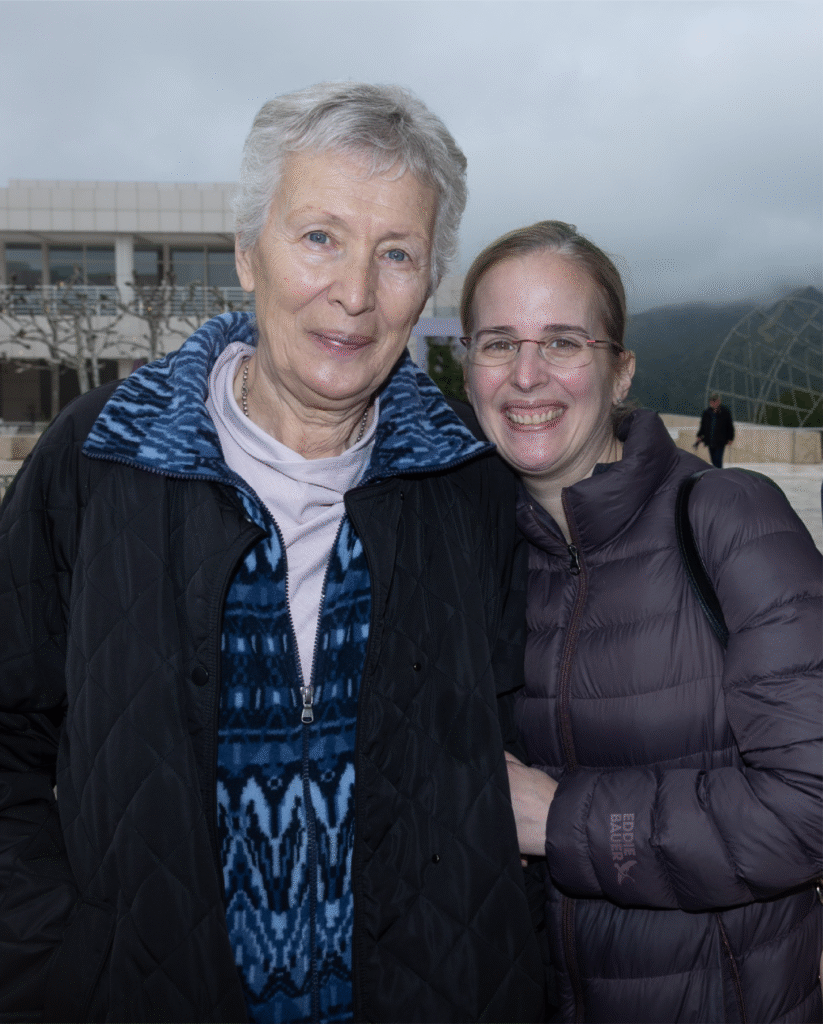 Two women outside in jackets smiling at camera. The one on the left is older.