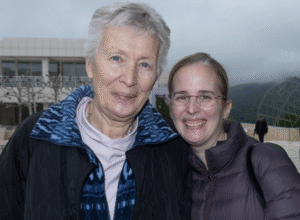 Two women outside in jackets smiling at camera. The one on the left is older.